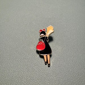 May include: Enamel pin featuring a cartoon character in a black dress, red bow, and red purse. The character is holding a bouquet of yellow flowers. The pin has a silver border and is set against a gray background.
