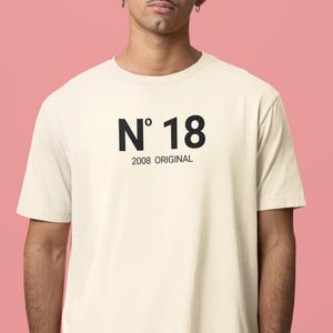 Può includere: Una t-shirt a maniche corte color crema con il testo nero N° 18 centrato sul petto. Sotto il numero, il testo 2008 ORIGINAL è stampato in un carattere nero più piccolo. Il capo presenta un classico girocollo e una vestibilità standard.