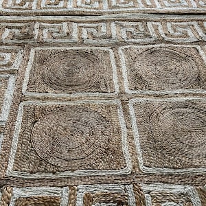 May include: A rectangular jute rug with a geometric design. The rug features a repeating pattern of squares and circles in shades of brown and beige. The border has a Greek key design.