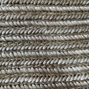 May include: Close-up of a woven rug with a textured surface. The rug is made of natural fibers, with a pattern of horizontal rows of tightly woven strands in shades of beige and gray.