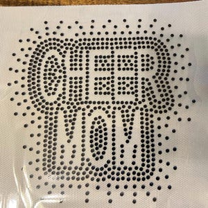 Peut inclure: Une feuille de tissu blanche avec les mots "GEEK MOM" épelés en strass noirs. Les strass sont disposés en motif de points, avec des points supplémentaires entourant le texte.