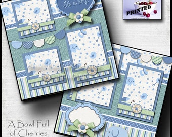 Può includere: Un design di carta per scrapbooking blu e verde con una cornice a forma di cuore che dice "È un maschio!" e uno striscione con cerchi blu e bianchi. La carta ha un motivo di stelle, elefanti e uccelli. La carta è stata progettata da A Bowl Full of Cherries ed è stampata.