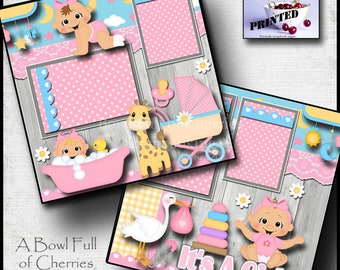 Könnte beinhalten: Ein rosa und blaues Scrapbook-Papier mit Holzmaserung. Das Papier zeigt verschiedene Baby-Motive, darunter ein Baby in der Badewanne, eine Giraffe, einen Kinderwagen, einen Storch und ein Baby-Mädchen. Der Text "It's A Girl" ist auf dem Papier gedruckt.