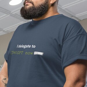 Puede incluir: Camiseta azul marino XL con el texto "I delegate to ChatGPT now" en verde. La camiseta tiene un sello redondo rojo que dice "XL Approved Finest Chaos or More".