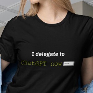 Puede incluir: Camiseta negra de cuello redondo con el texto "I delegate to ChatGPT now" en blanco y verde. La camiseta se lleva con una chaqueta vaquera.