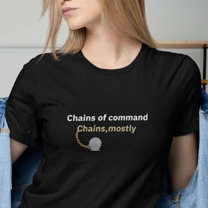 Peut inclure: T-shirt noir avec l'inscription "Chains of command Chains, mostly" en blanc et jaune. Un dessin d'un boulet et d'une chaîne est en dessous. Le t-shirt est de style col rond.