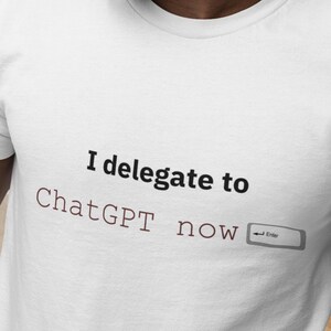 Puede incluir: Camiseta blanca con el texto "I delegate to ChatGPT now" en negro y granate. El diseño incluye un símbolo de la tecla Enter. La camiseta está hecha de un material suave.