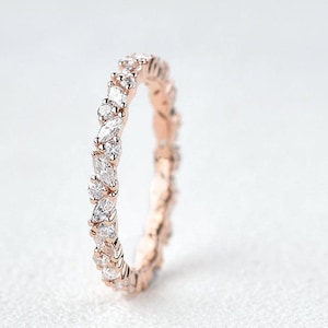 Peut inclure: Bague en or rose ornée d'une rangée continue de pierres précieuses claires, de taille marquise et ronde. La bague est posée sur un fond blanc, mettant en valeur l'éclat des pierres. Cette bague élégante est un bijou fin.