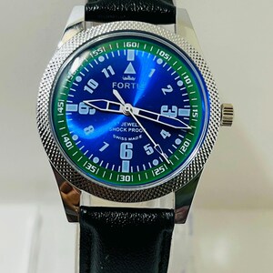 May include: A Fortis wristwatch with a blue sunray dial, white Arabic numerals, and luminous hands. The watch features a silver-toned textured bezel, a black leather strap, and text on the dial reading FORTIS, JEWELED, SHOCK PROOF, and SWISS MADE.