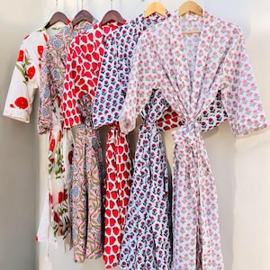 May include: A collection of colorful, patterned robes hanging on wooden hangers. The robes feature floral and fruit designs in red, pink, and blue on white backgrounds. The text "Jai Shree Shyam Store" is visible at the top.