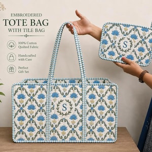 Puede incluir: Juego de bolso tote y bolso de azulejos bordados. Las bolsas presentan un estampado floral acolchado en azul, amarillo y verde sobre un fondo crema. El bolso tote tiene forma rectangular con asas a rayas azules y blancas. Una persona sostiene el bolso de azulejos.