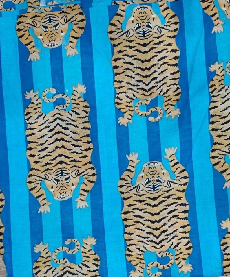 May include: Fabric with a repeating pattern of stylized tigers in tan and black stripes against a background of vertical blue stripes. The tigers are depicted in a playful, upright pose.