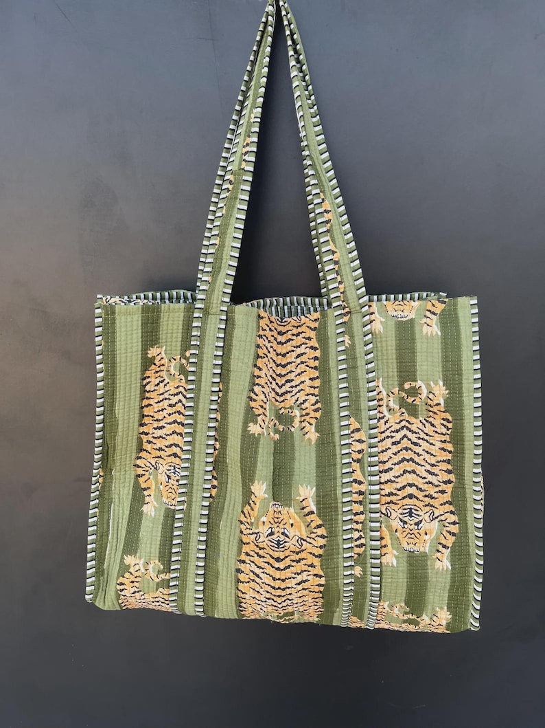 May include: Green tote bag with vertical stripes and tiger print. The bag features long handles and a rectangular shape. The tiger print is in shades of orange and black. The bag is made of a soft, quilted fabric.