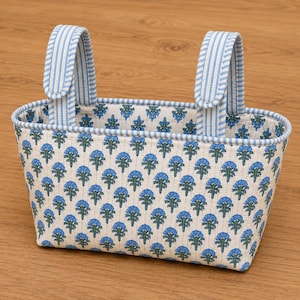 May include: A rectangular fabric storage basket featuring a repeating blue and green floral pattern on an off-white background. The basket includes two upright handles with a light blue and white vertical striped design and matching trim.