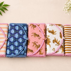 Peut inclure: Cinq articles en tissu pliés avec divers motifs et couleurs. Les motifs comprennent des rayures, des motifs floraux et des imprimés tigrés. Chaque article a une bordure rose et une fermeture à bouton. Les articles sont disposés en rangée.