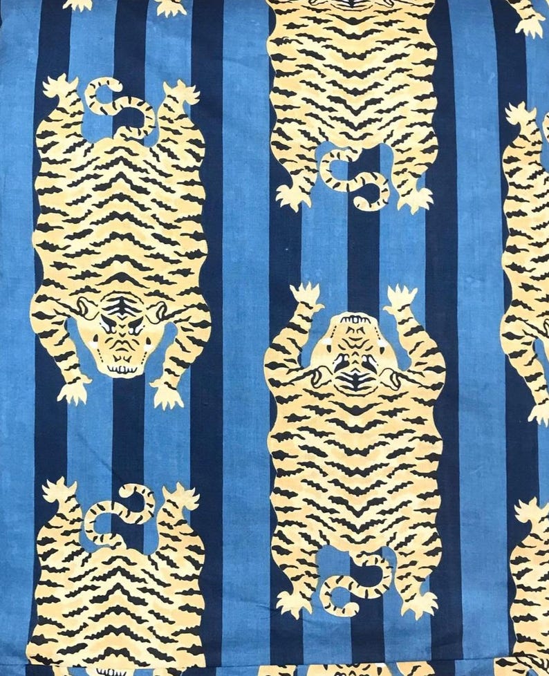 May include: Fabric with a repeating pattern of stylized tigers in cream and black against a blue and navy striped background. The tigers are depicted in a symmetrical pose, with their paws raised.