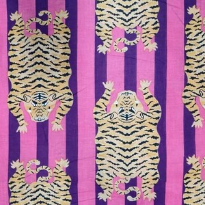 May include: Fabric with a repeating pattern of tigers in a vertical orientation. The tigers are tan with black stripes, set against a background of alternating pink and purple vertical stripes. The tigers are depicted with their paws up.
