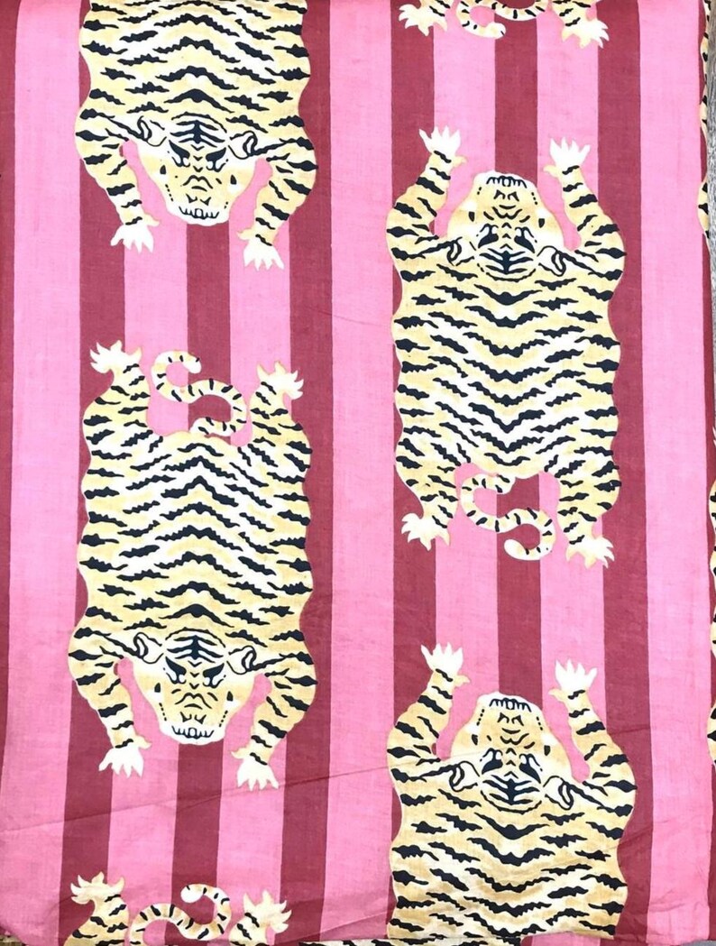 May include: A pink and burgundy striped fabric featuring a repeating pattern of stylized tigers. The tigers are yellow with black stripes and white accents. The fabric is likely used for home decor or apparel.