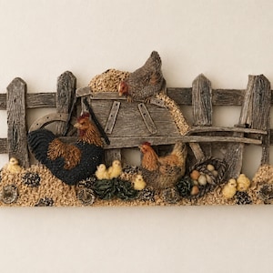 Peut inclure: Un porte-objets mural décoratif présentant une sculpture en relief d'une clôture en bois avec un coq, deux poules et plusieurs poussins. La scène comprend une brouette, un panier d'œufs et quatre crochets métalliques à la base.