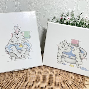Peut inclure: Deux impressions sur toile blanche rectangulaires présentant des illustrations de dessin animé d'un chat tigré gris dans une baignoire. Une impression montre le chat avec une petite souris sur la tête, l'autre le montre se relaxant avec une souris.