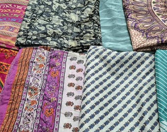 May include: A collection of folded fabrics featuring diverse patterns and colors, including a dark blue cloth, a pink and orange geometric print, a black and white elephant motif, a solid light blue piece, and a purple paisley textile.
