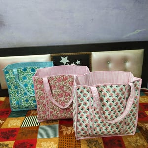May include: Three quilted tote bags with floral and striped patterns. One bag is teal with a floral design, and the other two are pink with floral patterns. The bags have matching handles and linings.
