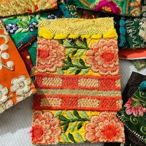 May include: Close-up of colourful embroidered fabric patches. The patches feature floral and geometric designs in shades of orange, yellow, green, and gold. The embroidery is detailed and intricate, with a variety of textures and patterns.