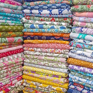 Könnte beinhalten: Stapel bunter Stoffe mit verschiedenen floralen und geometrischen Mustern. Die Stoffe sind in Blau-, Grün-, Rot-, Gelb- und Rosatönen gehalten. Das Bild zeigt eine Vielzahl von Textilien, wahrscheinlich für Bastelarbeiten oder Heimdekoration.