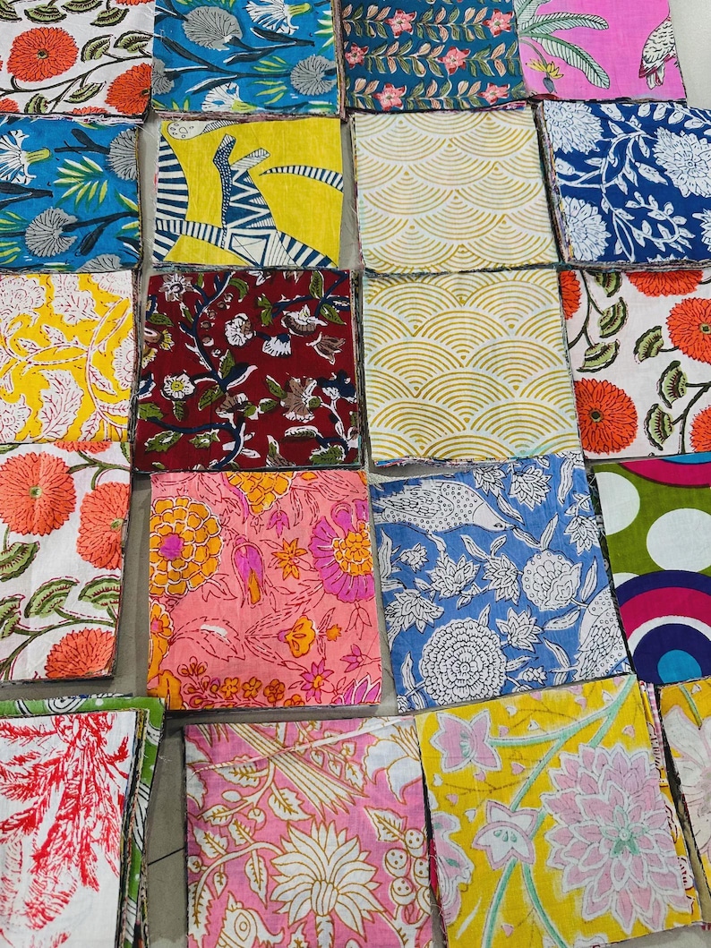 May include: A collection of colorful fabric squares with various floral and geometric patterns. The squares feature a range of colors, including blue, yellow, pink, and red, with detailed designs of flowers, leaves, and abstract shapes. The fabric appears to be cotton or a similar material.