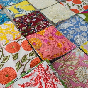 May include: A collection of folded fabric squares with various floral and geometric patterns. The fabrics feature a range of colors, including blue, yellow, red, and pink, with detailed designs. The arrangement showcases a variety of textile designs.