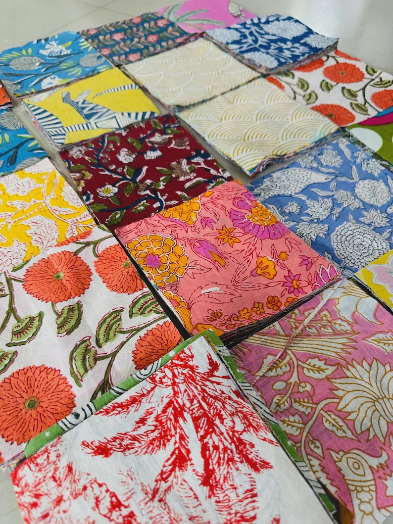 May include: A collection of folded fabric squares with various floral and geometric patterns. The fabrics feature a range of colors, including blue, yellow, red, and pink, with detailed designs. The arrangement showcases a variety of textile designs.