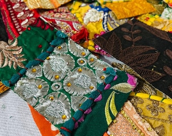 May include: Close-up of a collection of colorful fabric patches. The patches feature intricate embroidery, sequins, and various textures. Colors include green, gold, orange, and black. The patches are arranged in a layered, overlapping pattern.
