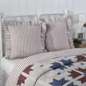 Könnte beinhalten: Zwei quadratische Kissen mit Rüschenkanten und einem gestreiften Muster in Weiß und Burgunderrot liegen auf einem Bett. Das Bett hat eine Steppdecke mit einem Sternmuster in Blau, Burgunderrot und Weiß. Das Kopfteil ist weiß.