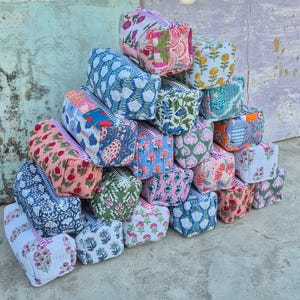 Può includere: Una pila di trousse per cosmetici colorate e decorate. Le trousse presentano vari disegni floreali e geometrici nei toni del rosa, blu, verde e bianco. Ogni trousse ha una chiusura a cerniera e una forma rettangolare.