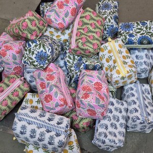 Può includere: Una collezione di trousse colorate con motivi floreali. Le borse presentano disegni floreali in rosa, blu, giallo e verde su sfondo bianco. Ogni borsa ha una chiusura a cerniera ed è di forma rettangolare o cilindrica.