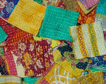 May include: A patchwork textile composed of numerous small, square fabric pieces in various colors and patterns. The squares are stitched together with white thread, creating a textured surface. The colors include yellow, green, red, and blue.
