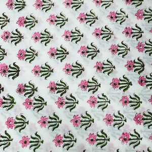 May include: White fabric with a repeating pattern of pink flowers and green leaves. The floral design is evenly spaced across the fabric, creating a visually appealing and symmetrical arrangement. The fabric appears to be cotton or a similar material.