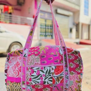 May include: A colourful patchwork duffel bag featuring floral and animal prints in shades of pink, red, and white. The bag has pink handles and a rectangular shape, suitable for travel or daily use.