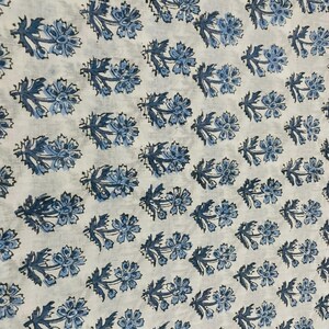 May include: White fabric with a repeating pattern of blue floral designs. The flowers have multiple petals and are arranged in rows. The leaves are a darker shade of blue.