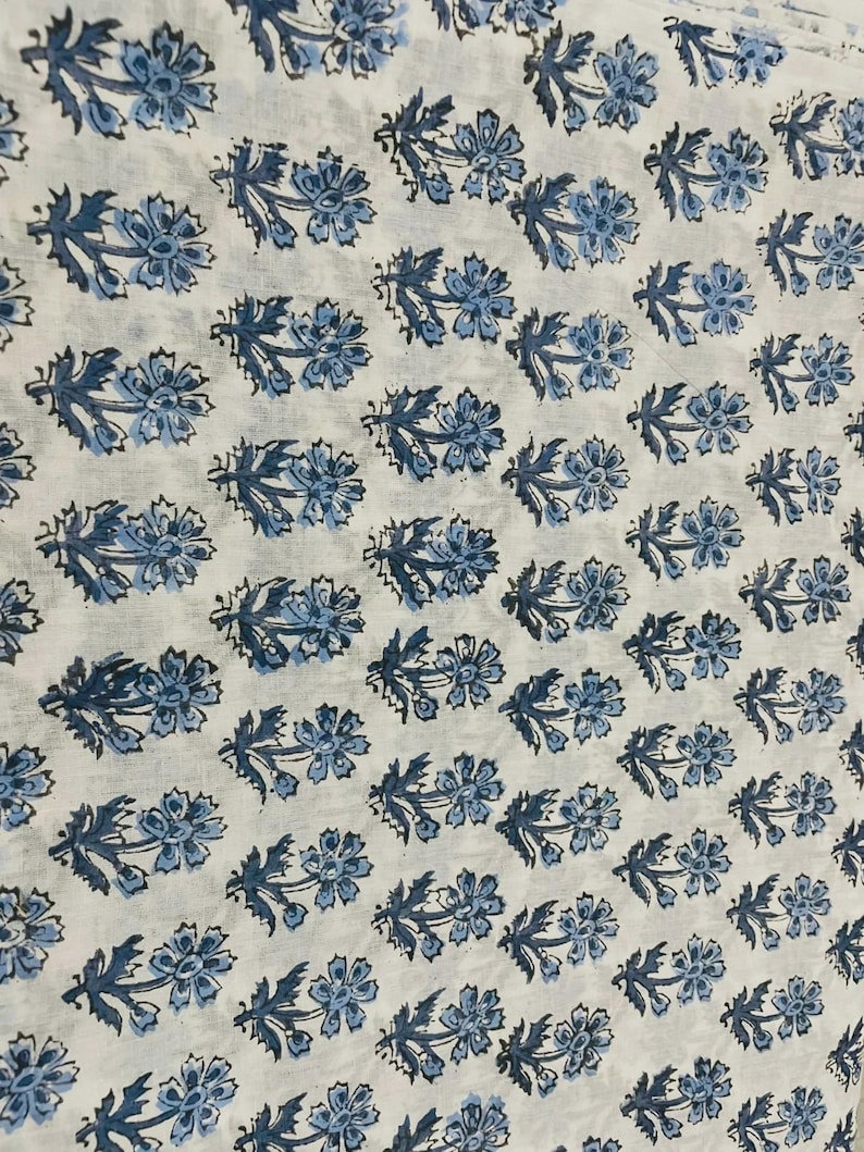 May include: White fabric with a repeating pattern of blue floral designs. The flowers have multiple petals and are arranged in rows. The leaves are a darker shade of blue.
