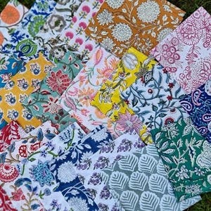 May include: A collection of colorful, patterned fabric squares. The fabrics feature floral and botanical designs in various colors, including blue, yellow, pink, and green. The patterns are detailed and intricate, creating a visually rich display.
