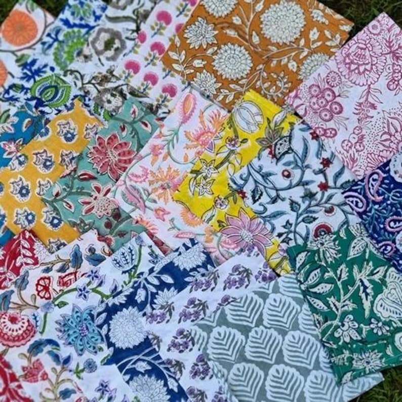May include: A collection of colorful, patterned fabric squares. The fabrics feature floral and botanical designs in various colors, including blue, yellow, pink, and green. The patterns are detailed and intricate, creating a visually rich display.