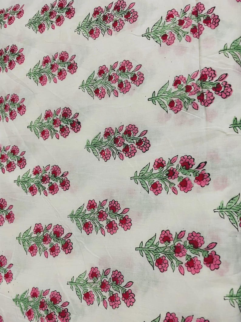 May include: White fabric with a repeating pattern of pink flowers and green leaves. The floral design is evenly spaced across the fabric, creating a visually appealing and symmetrical arrangement. The flowers are a vibrant pink, and the leaves are a soft green.