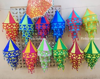 May include: A collection of colorful, cone-shaped lanterns with intricate patterns and mirrored accents. The lanterns are in various colors, including red, yellow, blue, and green, and are suspended from a string. A decorative umbrella is visible in the background.