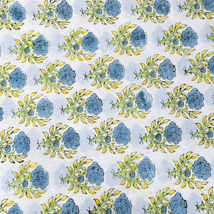 May include: White fabric with a repeating pattern of blue floral bouquets. Each bouquet features three blue flowers, green stems, and yellow leaves. The design is evenly spaced across the fabric.