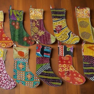 Könnte beinhalten: Eine Sammlung von zehn bunten Weihnachtsstrümpfen. Jeder Strumpf hat ein einzigartiges Patchwork-Design mit verschiedenen Mustern und Farben, darunter Rot, Grün, Gelb und Lila. Die Strümpfe sind aus Stoff und haben eine Schlaufe zum Aufhängen.