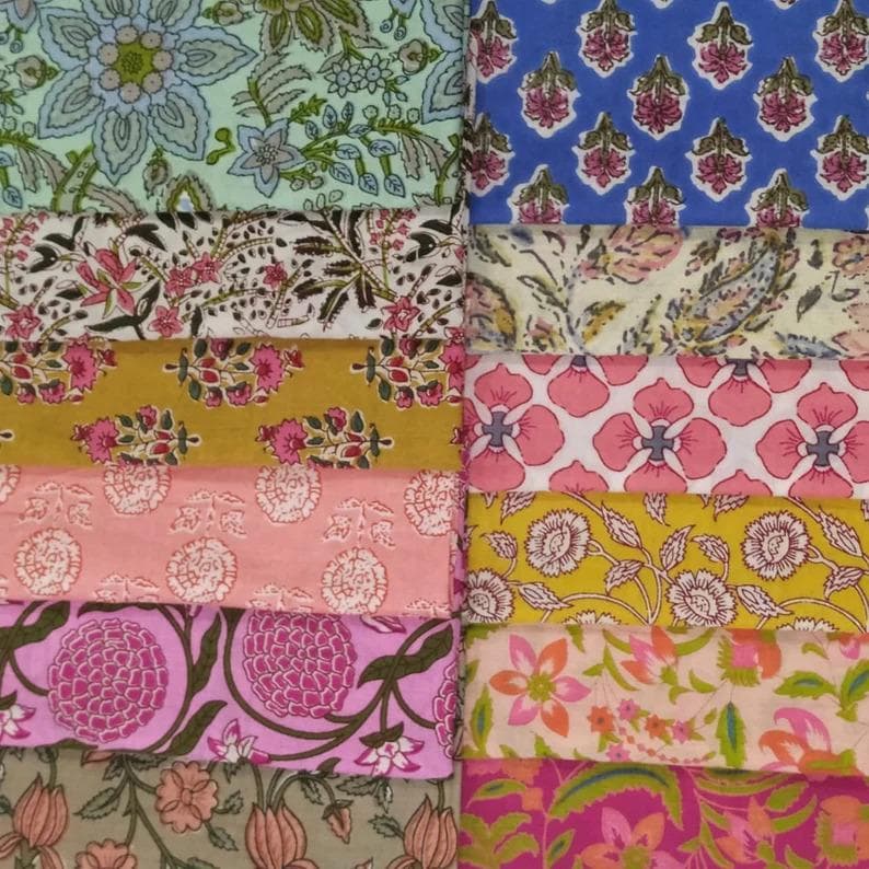 May include: A collection of colorful fabric swatches with floral patterns. The fabrics feature a variety of designs, including large and small flowers, leaves, and paisley motifs. Colors include blue, pink, yellow, and green.