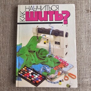 Può includere: Un libro di cucito con il titolo "Come imparare a cucire?" in russo. La copertina presenta una macchina da cucire, tessuto verde, un metro a nastro, rocchetti di filo e una rivista con forbici.