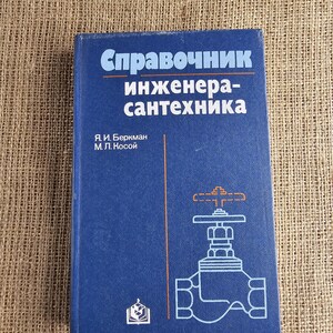 Op de afbeelding: Een blauw boek met de titel "Справочник инженера-сантехника" met witte en oranje tekst en een diagram van een klep. Het boek ligt op een getextureerd, bruin oppervlak.