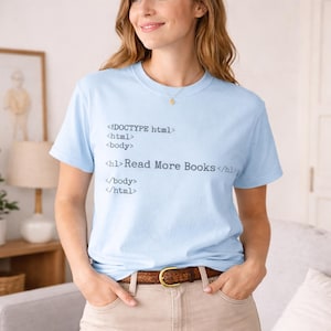 Könnte beinhalten: Eine weiße Keramik-Tasse mit schwarzem Henkel und dem Text "But First, Coffee" in schwarzer, handschriftlicher Schrift. Die Tasse steht auf einer weißen Oberfläche.